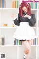 A woman in a maid outfit posing in front of a bookshelf.