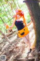 A woman dressed as a pumpkin holding a pitchfork in the woods.