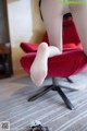 A woman in white stockings is sitting on a red chair.