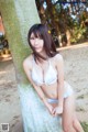 A woman in a white bikini leaning against a tree.