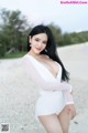 A woman in a white bodysuit posing on a beach.