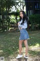 A woman in a denim skirt and white sneakers posing for a picture.