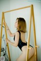 A woman in a black bodysuit leaning against a wooden ladder.