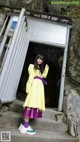 A woman in a yellow coat and purple skirt standing in front of a tunnel.