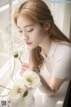 A woman sitting at a window sill with a vase of flowers.