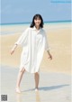 A woman in a white shirt dress walking on the beach.