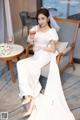 a woman in a white dress sitting on a chair holding a glass of wine