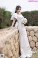 A woman in a wedding dress leaning against a stone wall.