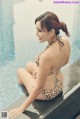 A woman in a leopard print bikini sitting by a swimming pool.