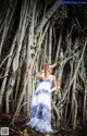 A woman in a blue and white dress standing in front of a tree.