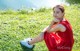 A woman in a red dress sitting on the grass.