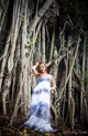 A woman in a blue and white dress standing in front of a tree.