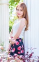 A woman leaning against a white wall with flowers in her skirt.