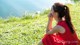 A woman in a red dress sitting on the grass by the water.