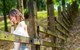 A woman leaning against a wooden fence in the woods.