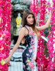 A woman in a floral dress standing in front of pink flowers.