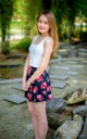 A woman in a white tank top and floral skirt posing for a picture.