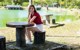 A woman sitting on top of a wooden table next to a lake.