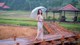 A woman standing on a wooden bridge holding an umbrella.