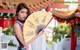 A woman in a cheongsam holding a fan in front of a temple.