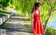 A woman in a red dress standing on a sidewalk next to a lake.