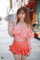 A woman in a pink top and orange skirt taking a selfie.