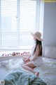 A woman sitting on a bed in front of a window.