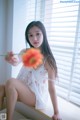 A woman sitting on a window sill holding a flower.