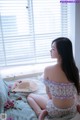 A woman sitting on a bed in front of a window.