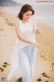 A woman in a white top and blue pants on a beach.