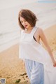 A woman in a white top and blue pants on the beach.