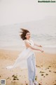 A woman in a white dress is dancing on the beach.