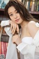 A woman leaning on a chair in front of a bookshelf.