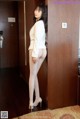 A woman in a white suit leaning against a wooden door.