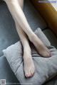 A woman's legs are sitting on a pillow on a couch.