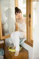 A woman sitting on top of a dresser next to a window.