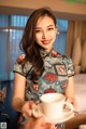 A woman in a cheongsam holding a cup of coffee.