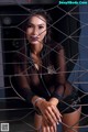 A woman in a black leather outfit is posing behind a fence.