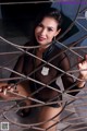 A woman in a black leather outfit is posing behind bars.