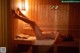 A naked woman laying on a wooden bench in a sauna.