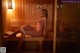 A naked woman sitting on a bench in a sauna.