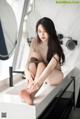 A woman sitting on top of a white counter next to a mirror.