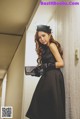 A woman in a black dress leaning against a wall.