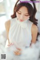 A woman in a white dress sitting on a bed.