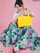 A woman sitting on a pink background holding a yellow bag.