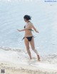 A woman in a black bikini walking on the beach.