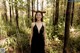 A woman in a black dress standing in the woods.