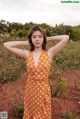 A woman in an orange polka dot dress standing in a field.