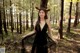 A woman in a black dress standing in the woods.