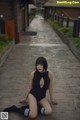 A woman in a black bodysuit sitting on a wooden walkway.